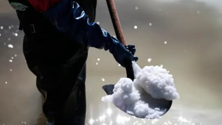 Un trabajador utiliza una pala para mostrar la materia prima para la fabricación de carbonato de litio dentro de una piscina de recuperación de sal en la planta piloto de Llipi en el Salar de Uyuni, en Bolivia, el 13 de agosto de 2022. (Gaston Brito Miserocchi/Getty Images)
