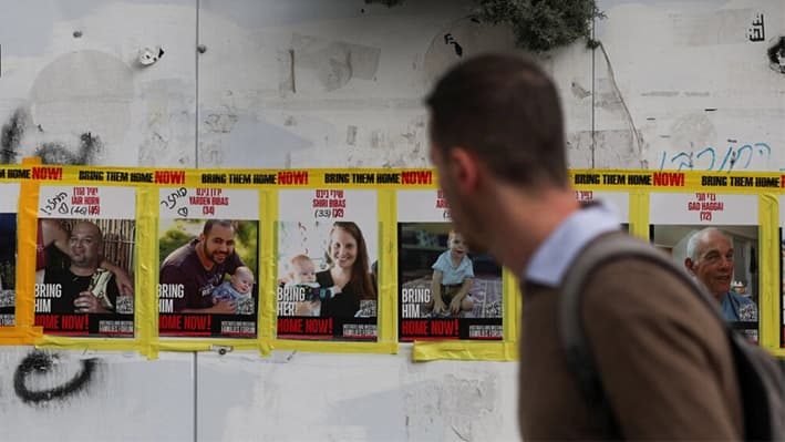Un hombre pasa junto a las fotos de Yarden Bibas, Shiri Bibas y Kfir Bibas en Jerusalén, Israel, el 19 de febrero de 2025. (Ronen Zvulun/Reuters)
