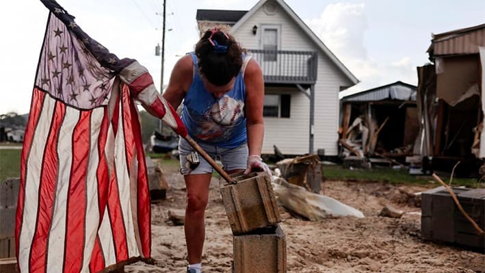 Roxanne Brooks monta una bandera estadounidense en una pila de bloques de hormigón frente a la casa móvil destruida de su amiga (D) tras las inundaciones provocadas por el huracán Helene en Swannanoa, Carolina del Norte, el 6 de octubre de 2024. (Mario Tama/Getty Images)
