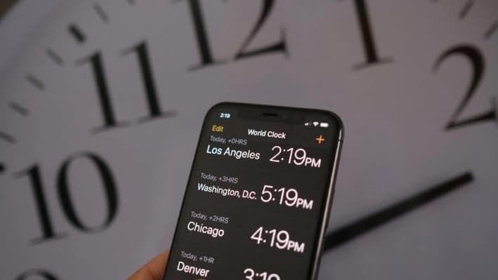 Un reloj detrás de un teléfono inteligente que muestra la hora después de que se implementara el horario de verano, en Los Ángeles, el 15 de marzo de 2022. (Chris Delmas/AFP vía Getty Images)