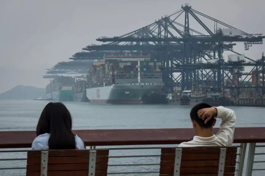 Un hombre y una mujer sentados en un banco frente a la Terminal Internacional de Contenedores de Yantian, donde enormes buques portacontenedores están atracados bajo hileras de grúas pórtico, en Shenzhen, China, el 11 de abril de 2025. (Cheng Xin/Getty Images)