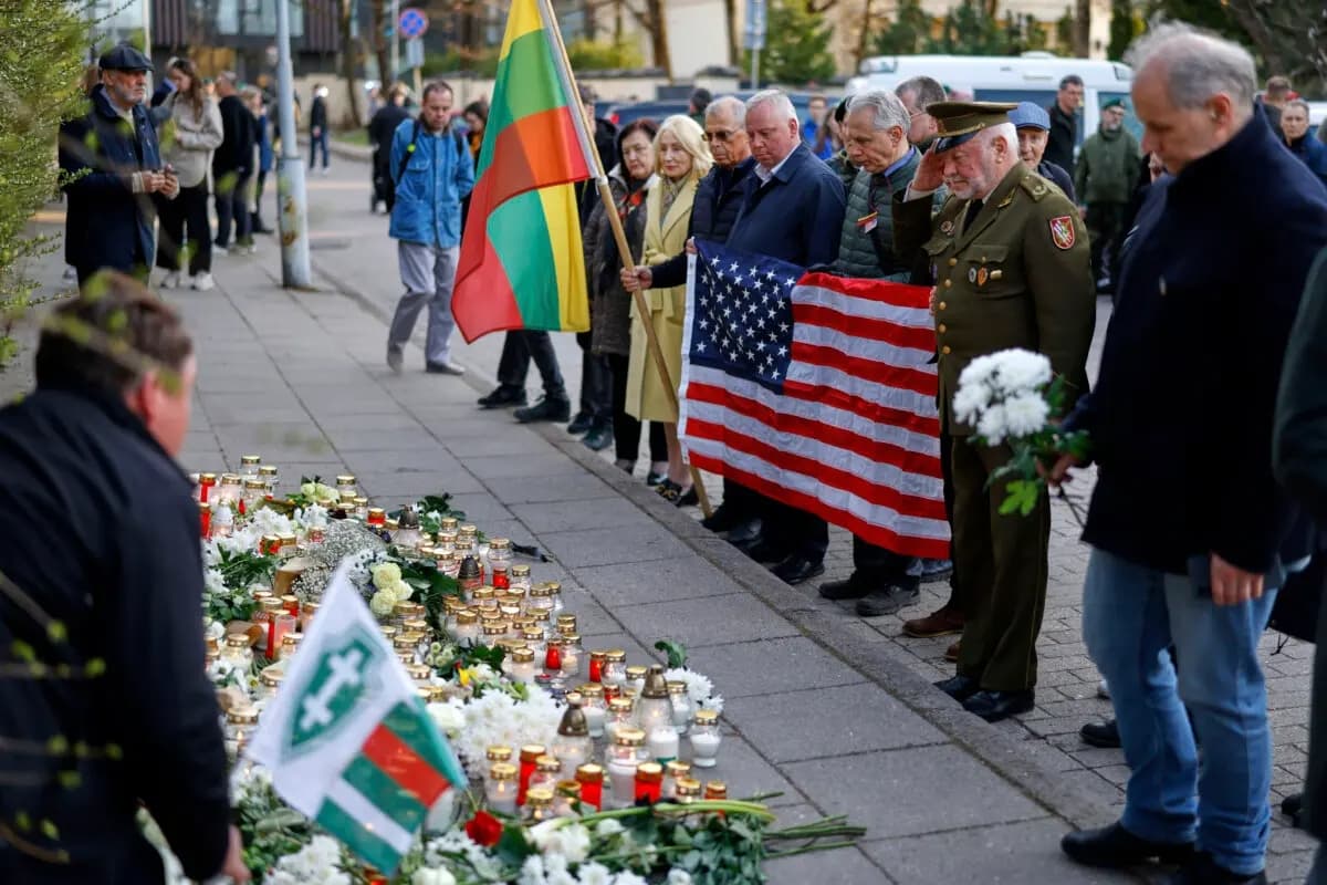 Personas con la bandera nacional de EE. UU. acuden a presentar sus últimos respetos a los tres soldados encontrados muertos el lunes en un campo de entrenamiento en Pabrade, cerca de la embajada de EE. UU. en Vilna, Lituania, el 1 de abril de 2025. (Mindaugas Kulbis/AP Photo)