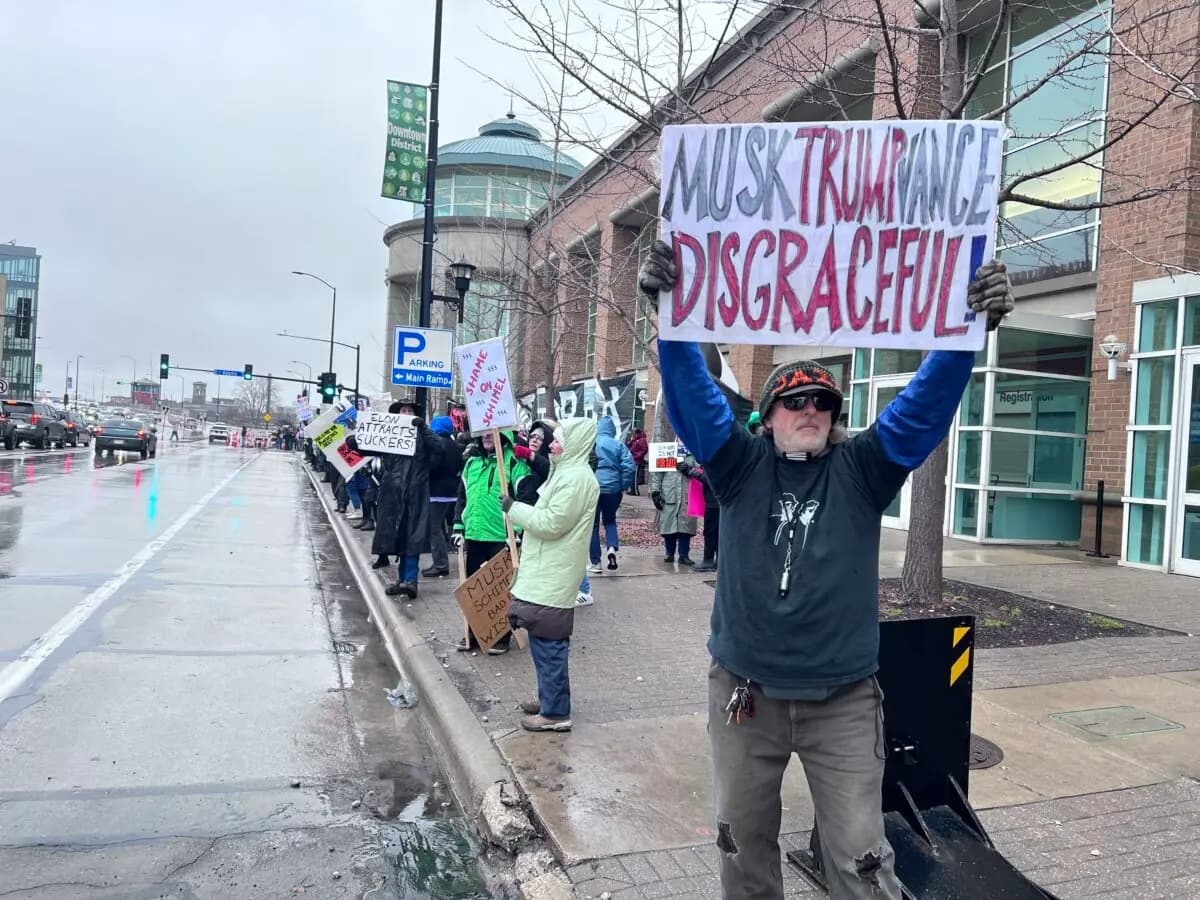 Un hombre muestra una pancarta de protesta frente a una reunión municipal organizada por Elon Musk en Green Bay, Wisconsin, el 30 de marzo de 2025. (Lawrence Wilson/The Epoch Times)