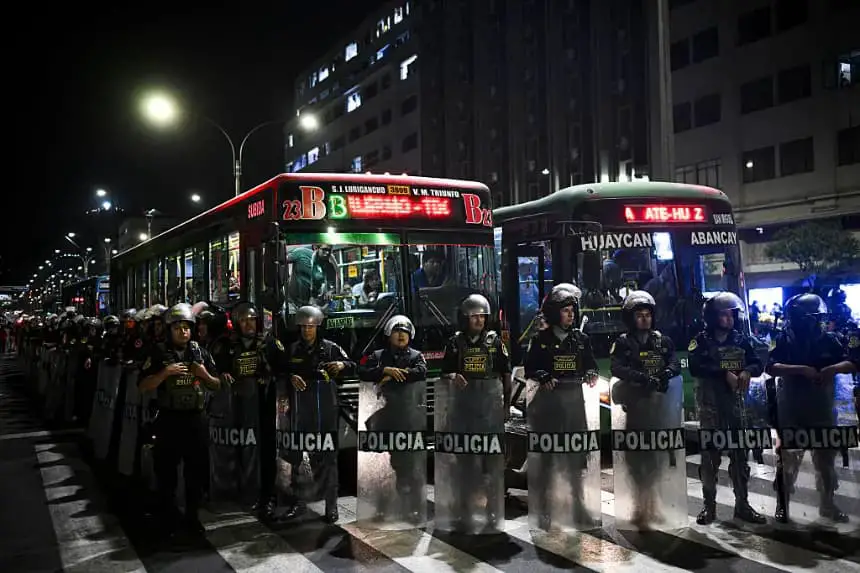 Personas dentro del transporte público esperan mientras agentes de policía antidisturbios hacen guardia frente a ellos durante una protesta contra el Gobierno por el crimen organizado y los sicarios en Lima (Perú) el 28 de marzo de 2025. (Ernesto Benavides/AFP vía Getty Images)
