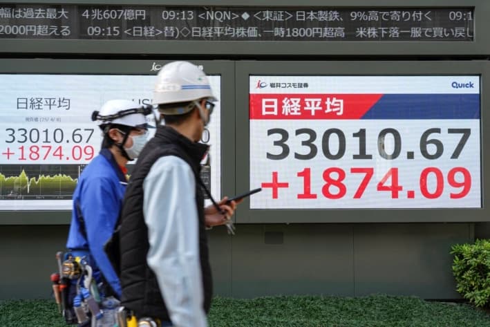 Empleados pasan junto a un tablero electrónico que muestra las cifras del Nikkei Stock Average en la Bolsa de Tokio, en una calle de Tokio, el 8 de abril de 2025. (Kazuhiro Nogi/AFP)