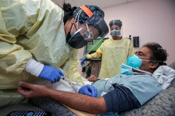 La enfermera Salina Padilla (izquierda) prepara al Dr. Prabakar Tummala para la infusión de anticuerpos monoclonales Bamlanivimab en el Hospital Desert Valley de Victorville, California, el 17 de diciembre de 2020. (Irfan Khan/Los Angeles Times/TNS)
