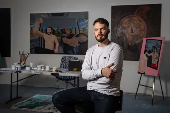 Andrei Kozlov, un rehén rescatado y tomado por Hamás cuando estaba en el festival de música Nova en octubre de 2023, posa con algunas de sus obras de arte, incluyendo «Autopista al infierno» (izq.) en un estudio en la ciudad de Nueva York, el 24 de abril de 2025. (Samira Bouaou/The Epoch Times)