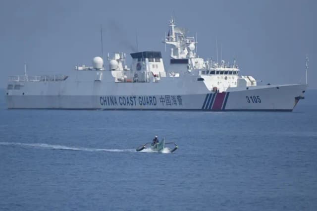 Esta foto, tomada el 20 de septiembre de 2023, muestra a un pescador filipino a bordo de su bote de madera navegando junto a un buque de la guardia costera china cerca del banco de arena Scarborough, controlado por China, en aguas disputadas del Mar de China Meridional. (Ted Aljibe/AFP vía Getty Images)