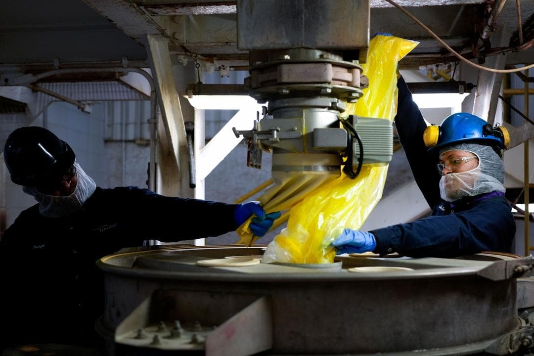Jobe Washington y Dwight Brown utilizan un gran tamiz para mezclar un tono de color amarillo en Sensient Technologies Corp., una empresa de fabricación de aditivos colorantes, en St. Louis, el 2 de abril de 2025. (Jeff Roberson/AP Photo)