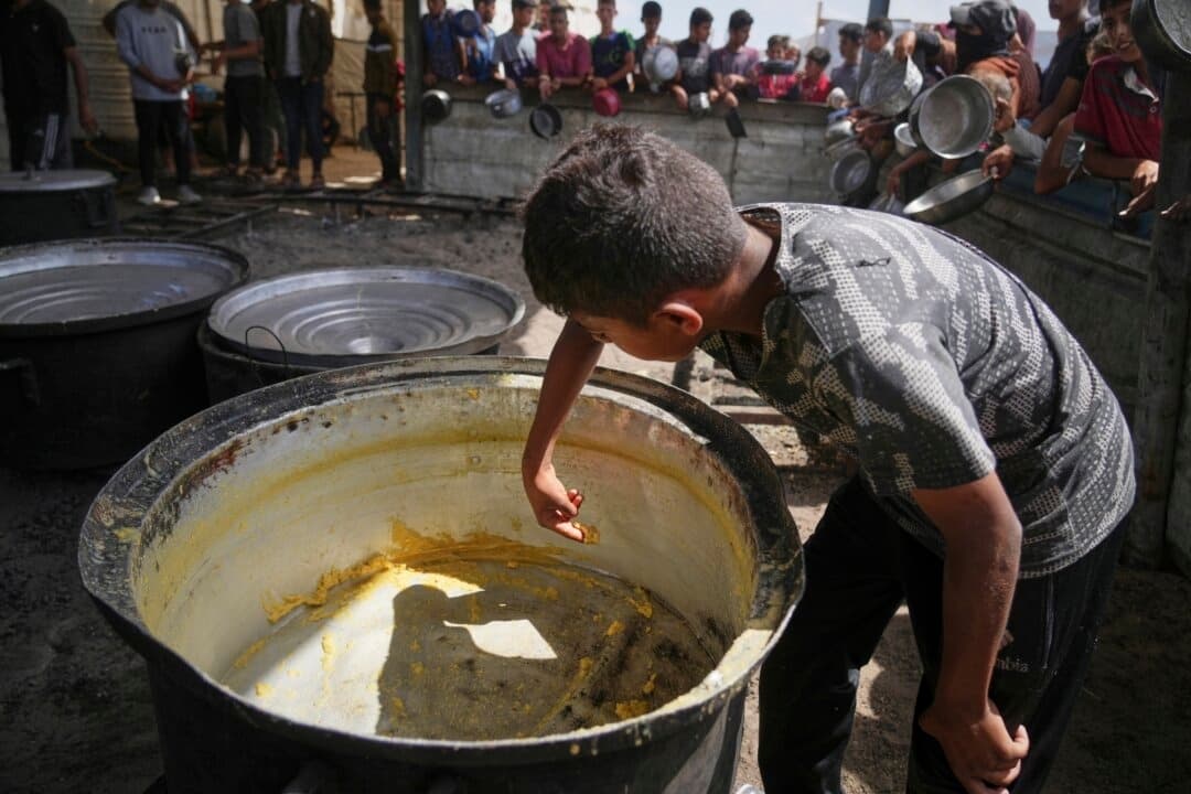 Un niño raspa los restos de una olla vacía después de que se distribuyeran todas las comidas en un comedor comunitario en Khan Younis, en el sur de la Franja de Gaza, el 14 de mayo de 2025. (Abdel Kareem Hana/AP)
