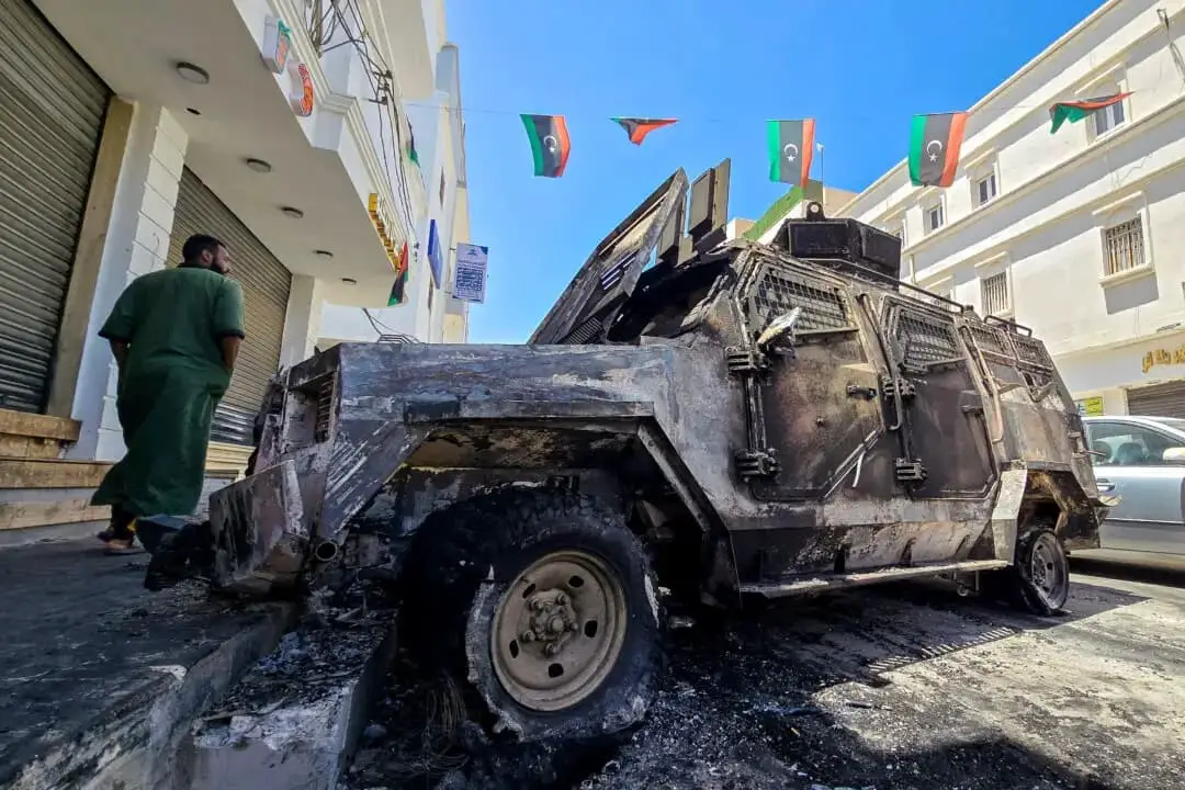Un hombre pasa junto a un coche destruido durante los enfrentamientos nocturnos en el distrito sureño de Abu Salim, en Trípoli (Libia), el 13 de mayo de 2025. (Mahmud Turkia/AFP a través de Getty Images)