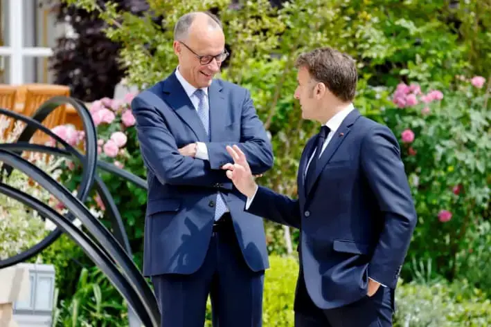 El presidente francés, Emmanuel Macron (der.), habla con el canciller alemán, Friedrich Merz, en el jardín del Palacio del Elíseo, en París, el 7 de mayo de 2025. (Ludovic Marin/Reuters)