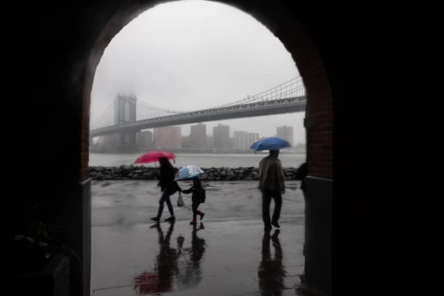La gente camina bajo la lluvia frente al horizonte de Manhattan cubierto por la niebla en la ciudad de Nueva York el 6 de mayo de 2025. (Spencer Platt/Getty Images).