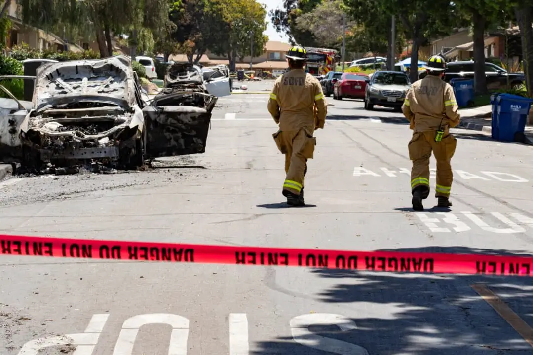 Los bomberos inspeccionan una calle residencial donde varios autos estacionados se incendiaron cuando un pequeño avión se estrelló el 22 de mayo de 2025. (Jane Yang/The Epoch Times).