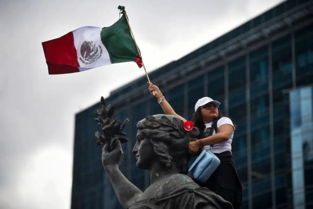 Una mujer sostiene una bandera mexicana mientras participa en una protesta tras la aprobación por el Senado de la reforma judicial propuesta por el gobierno en la glorieta del Ángel de la Independencia en la Ciudad de México el 11 de septiembre de 2024.  (RODRIGO OROPEZA/AFP vía Getty Images)