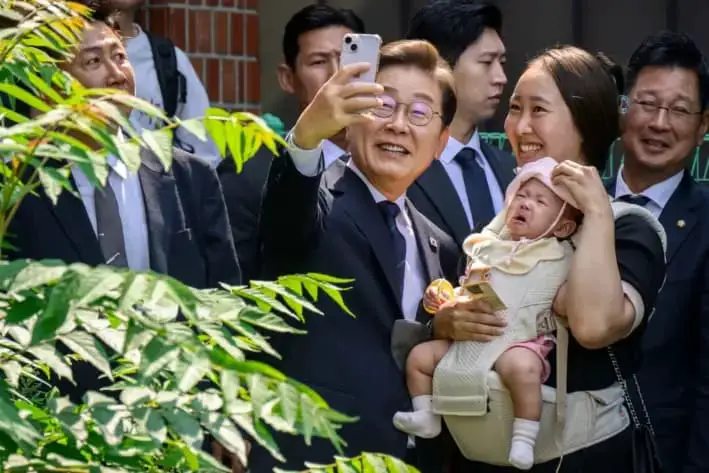 Lee Jae-myung (centro), candidato presidencial del Partido Democrático de Corea del Sur, se toma una selfi con un simpatizante a la salida de un colegio electoral tras emitir su voto anticipado, en Seúl, el 29 de mayo de 2025. (Anthony Wallace/AFP vía Getty Images)
