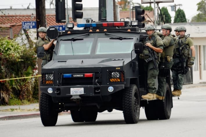 Miembros del equipo SWAT del Sheriff del Condado de Los Ángeles, de pie sobre un vehículo blindado, llegan para ayudar a los oficiales del Departamento de Policía de Los Ángeles durante una búsqueda masiva de un sospechoso que intentó matar a dos detectives, en Los Ángeles, el 25 de junio de 2013. (Kevork Djansezian/Getty Images)