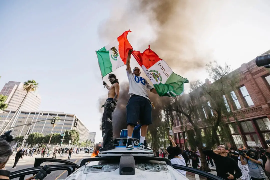 Dos manifestantes ondean banderas mexicanas mientras se suben a un vehículo vandalizado de Waymo durante una manifestación en Los Ángeles el 8 de junio de 2025. (David Pashaee/Middle East Images/AFP a través de Getty Images)