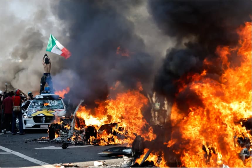 Un manifestante sostiene una bandera mexicana mientras autos en llamas se alinean en la calle en Los Ángeles, California, el 8 de junio de 2025. (Mario Tama/Getty Images)