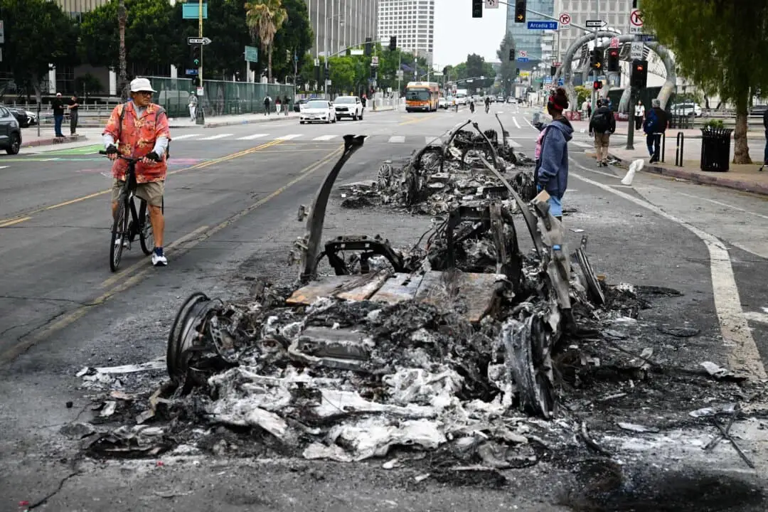 La gente observa los restos carbonizados de un vehículo quemado en la calle tras una noche de protestas en respuesta a las operaciones federales de inmigración en Los Ángeles, el 9 de junio de 2025. (Ronaldo Schemidt/AFP vía Getty Images).