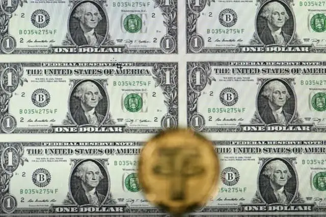 Una moneda de criptomoneda Tether (USDT) de oro macizo colocada junto a una pantalla que muestra billetes de dólar estadounidense en una ilustración tomada en Londres el 8 de mayo de 2022. (Justin Tallis/AFP a través de Getty Images)
