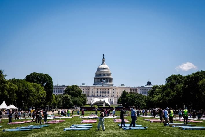 Personas contemplan secciones de la colcha «Freedom to Be» (Libertad de ser) extendida sobre el césped del National Mall durante la inauguración del World Pride, en Washington, el 17 de mayo de 2025. (Samuel Corum/Getty Images)