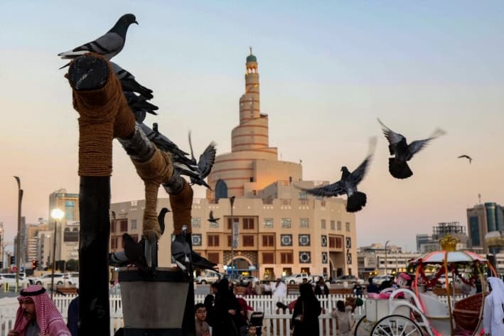 Palomas posadas en un pozo de agua decorativo fuera del Bazar Souq Waqif, con la mezquita Fanar y el Centro Cultural Islámico Abdulla Bin Zaid Al-Mahmoud al fondo, en Doha, Qatar, el 5 de diciembre de 2024. (KARIM JAAFAR/AFP vía Getty Images)
