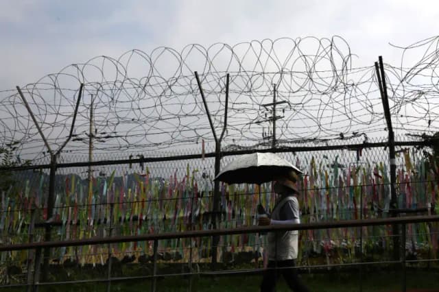 Una mujer camina junto a cintas de oración deseando la reunificación de las dos Coreas en la cerca de alambre en el Pabellón Imjingak, cerca de la zona desmilitarizada (DMZ) el 19 de julio de 2023 en Paju, Corea del Sur. (Chung Sung-Jun/Getty Images)