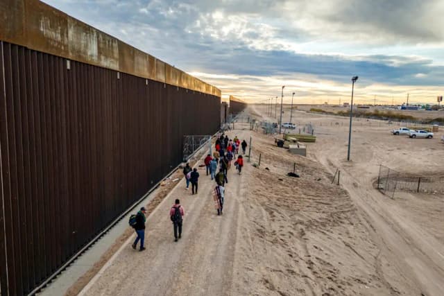 Inmigrantes ilegales caminan junto al muro fronterizo entre Estados Unidos y México tras cruzar el río Grande hacia El Paso, Texas, el 1 de febrero de 2024. (John Moore/Getty Images)
