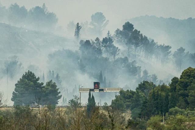 Esta fotografía muestra una señal de advertencia iluminada parpadeando mientras el humo se eleva desde un incendio en el costado de la autopista A6 durante un incendio forestal cerca de Moux, en el suroeste de Francia, el 5 de julio de 2025. (Idriss Bigou-Gilles/AFP vía Getty Images)