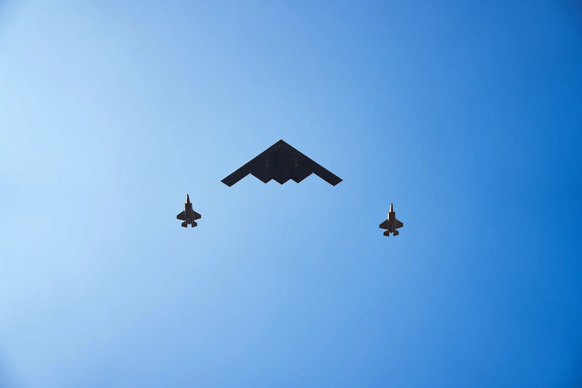 Bombarderos B-2 Spirit sobrevuelan la Casa Blanca mientras el presidente Donald Trump se pone de pie para escuchar el Himno Nacional durante un picnic familiar militar por el Día de la Independencia en el jardín sur de la Casa Blanca en Washington el 4 de julio de 2025. (Eric Lee/Getty Images)