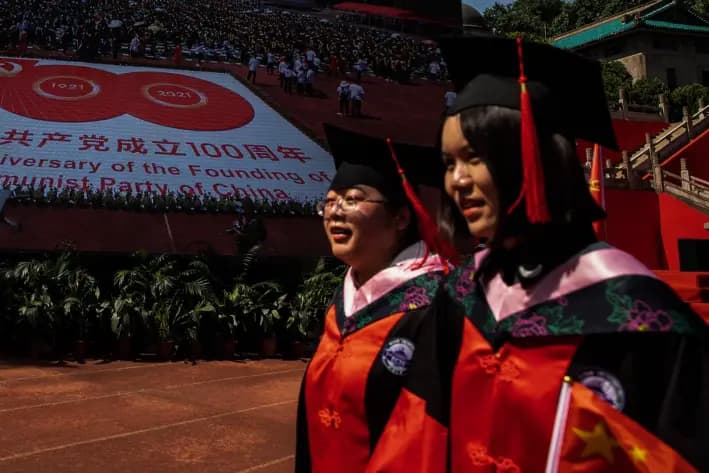 Dos graduados pasan ante pantallas que muestran el centenario del Partido Comunista Chino en la Universidad de Wuhan, China, el 23 de junio de 2021. (Getty Images)