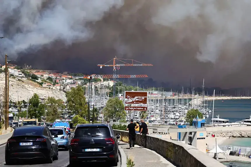 La gente observa cerca de la Plage des Corbières, en Marsella, sur de Francia, el 8 de julio de 2025, mientras el humo de un incendio forestal se extiende al fondo. (Clement Mahoudeau/AFP vía Getty Images)