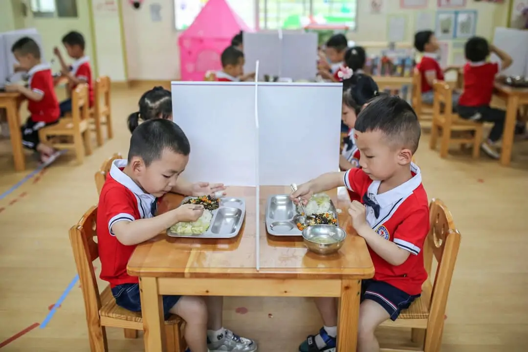Niños almorzando en mesas con divisiones plásticas en un kínder de Yongzhou, en la provincia central de Hunan, China, el 11 de mayo de 2020. (STR/AFP vía Getty Images)