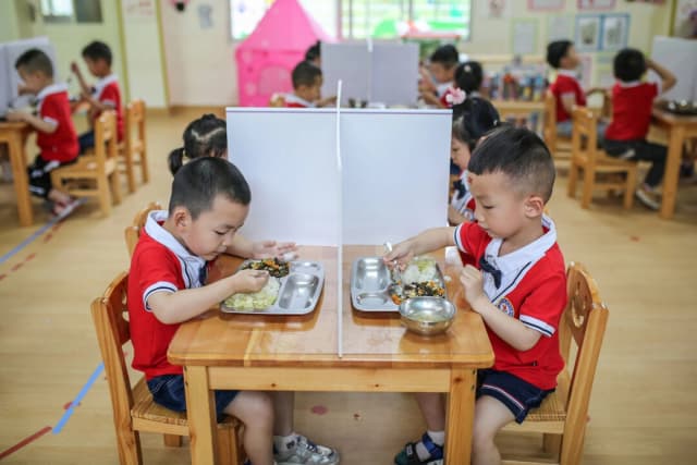 Niños almorzando en mesas con divisiones plásticas en un kínder de Yongzhou, en la provincia central de Hunan, China, el 11 de mayo de 2020. (STR/AFP vía Getty Images)