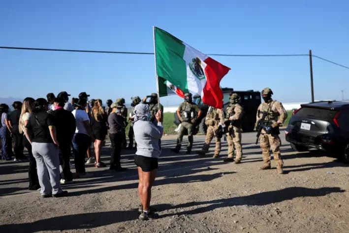 Un manifestante sostiene banderas mexicanas mientras agentes federales bloquean una carretera que conduce a una granja de marihuana donde agentes federales y oficiales de inmigración llevaron a cabo un operativo, en Camarillo, California, el 10 de julio de 2025. (Daniel Cole/Reuters)