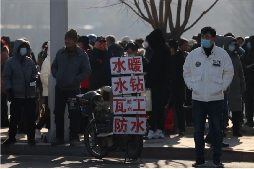 Trabajadores migrantes esperan junto a carteles que anuncian sus habilidades en una calle para ser contratados en Shenyang, provincia de Liaoning, al noreste de China, el 6 de febrero de 2023. (AFP vía Getty Images)