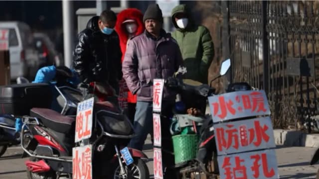 Trabajadores migrantes esperan cerca de carteles que anuncian sus habilidades mientras esperan en una calle para ser contratados en Shenyang, en la provincia de Liaoning, al noreste de China, el 6 de febrero de 2023. (STR/AFP vía Getty Images)