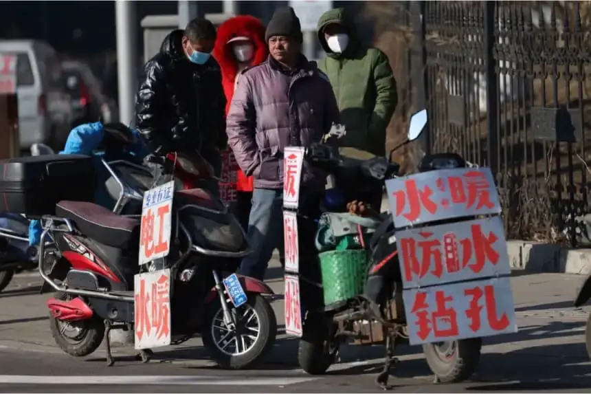 Trabajadores migrantes esperan cerca de carteles que anuncian sus habilidades mientras esperan en una calle para ser contratados en Shenyang, en la provincia de Liaoning, al noreste de China, el 6 de febrero de 2023. (STR/AFP vía Getty Images)
