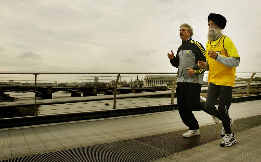 Fauja Singh (Dcha.), de 93 años, el corredor de mayor edad de la maratón Flora de Londres del 2004, corre por el Puente del Milenio en Londres junto a David Bedford, director de la maratón Flora de Londres, el 1 de abril de 2004, tras recibir un premio en reconocimiento a sus extraordinarios logros en el mundo del atletismo y celebrar su 93.º cumpleaños. (JIM WATSON/AFP a través de Getty Images)
