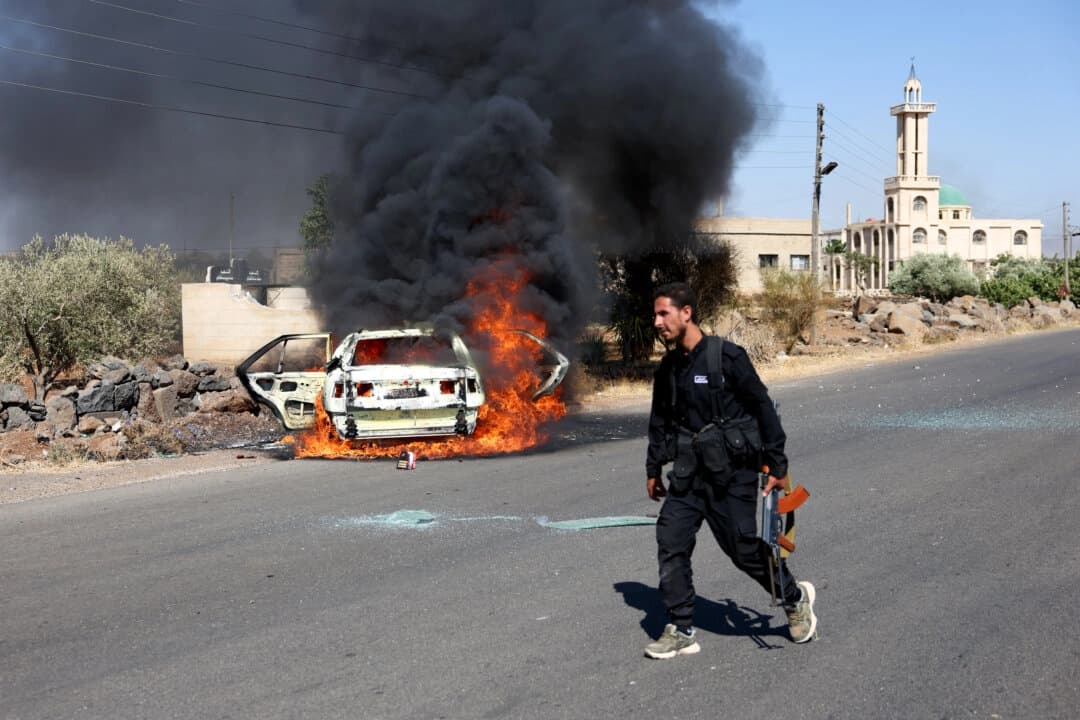 Un hombre armado pasa junto a un vehículo en llamas cerca del lugar donde se han producido enfrentamientos entre drusos y beduinos cerca de Sweida, Siria, el 14 de julio de 2025. (Stringer/Getty Images).