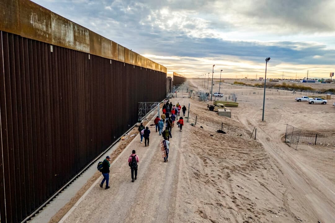 Inmigrantes ilegales caminan junto al muro fronterizo entre Estados Unidos y México después de cruzar el Río Grande hacia El Paso, Texas, el 1 de febrero de 2024. (John Moore/Getty Images)
