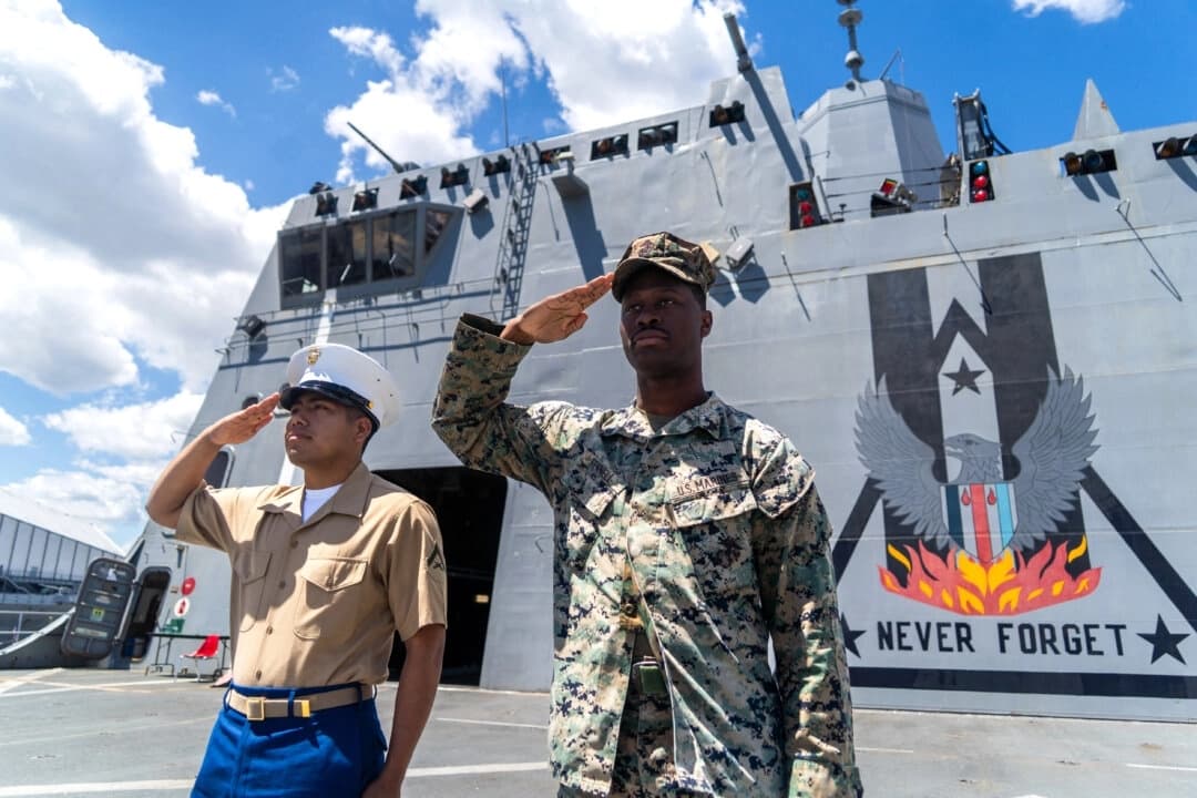 Un marine estadounidense y un marinero de la Armada de los Estados Unidos saludan frente a un mural con la leyenda "NEVER FORGET" a bordo del helipuerto del USS New York durante los actos conmemorativos del Memorial Day, en el último día de la Fleet Week en Manhattan, Nueva York, el 26 de mayo de 2025. (Hans Lucas/AFP a través de Getty Images)
