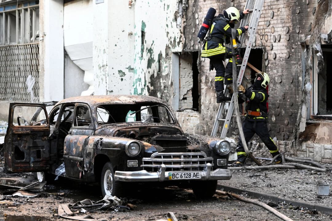 Bomberos junto a un auto quemado tras los ataques con drones y misiles rusos en la ciudad ucraniana de Lviv el 12 de julio de 2025. (YURIY DYACHYSHYN/AFP vía Getty Images).