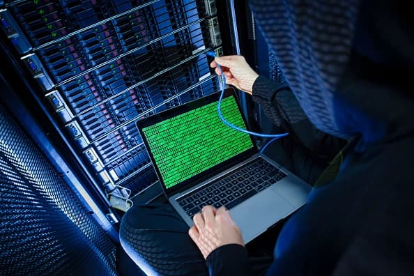 En esta foto de archivo, un hombre posa con una computadora portátil que muestra un código binario frente a los racks de servidores de un centro de servidores. (Thomas Trutschel/Photothek vía Getty Images)
