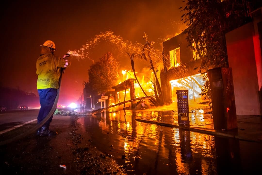 Un bombero lucha contra el incendio Palisades Fire, que quema viviendas en la autopista Pacific Coast Highway durante una fuerte tormenta de viento en Los Ángeles, el 8 de enero de 2025. (Apu Gomes/Getty Images)

