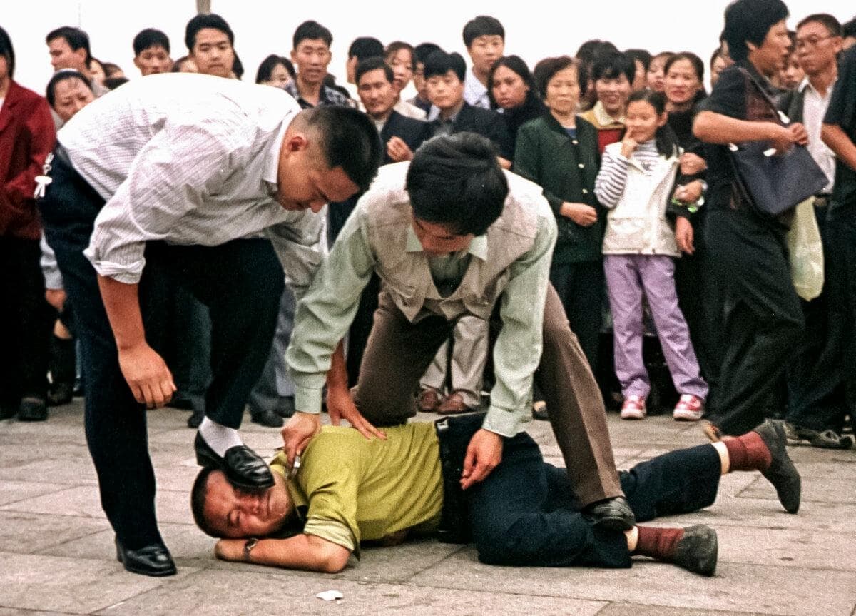 La policía detiene a un practicante de Falun Gong mientras se reúne una multitud en la plaza de Tiananmen, en Beijing, el 1 de octubre de 2000. (Chien-Min Chung/AP Photo)