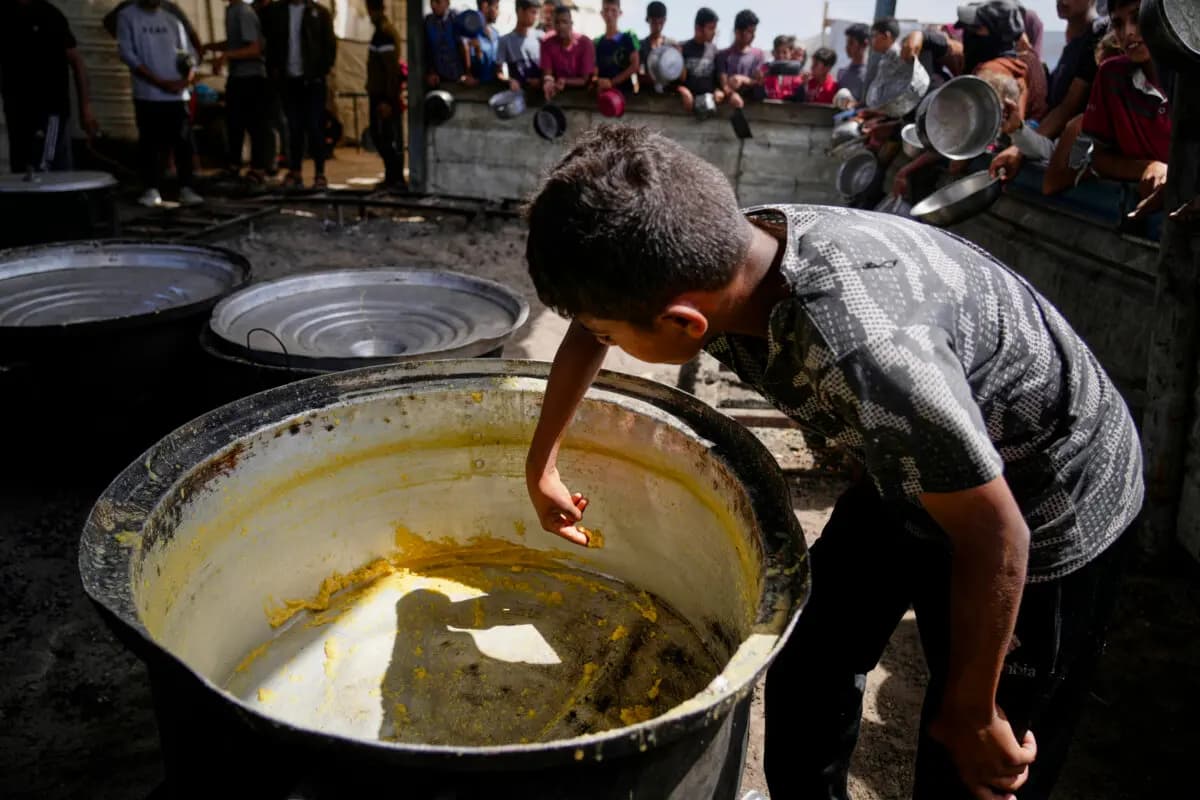 Un niño raspa los restos de una olla vacía después que se distribuyera toda las comida en un comedor comunitario en Khan Younis, en el sur de la Franja de Gaza, el 14 de mayo de 2025. (Abdel Kareem Hana/AP)
