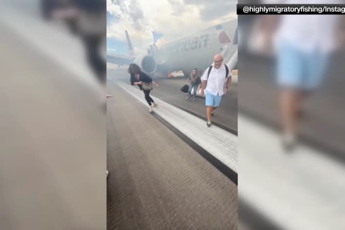 Pasajeros evacuan un avión de American Airlines en la pista del Aeropuerto Internacional de Denver el 26 de julio de 2025, mientras una columna de humo sale de la parte inferior del avión. (@highlymigratoryfishing vía Instagram vía Reuters/Captura de pantalla vía The Epoch Times)