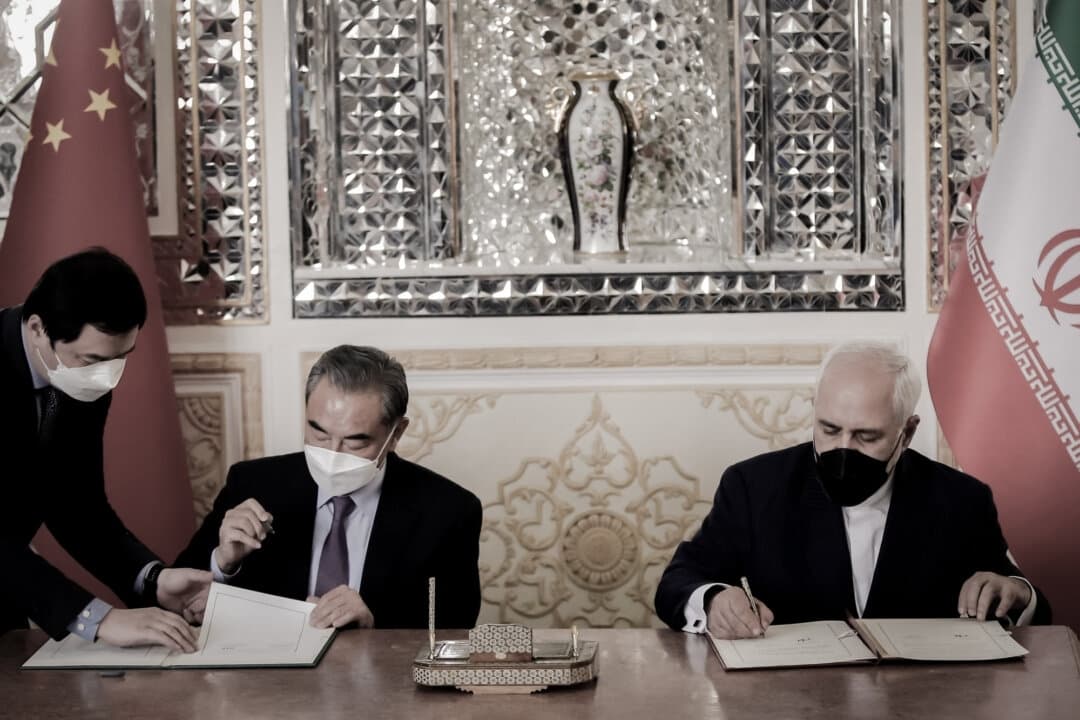El ministro de Asuntos Exteriores iraní, Mohammad Javad Zarif (derecha), y su homólogo chino, Wang Yi (centro), firman un acuerdo en la capital iraní, Teherán, el 27 de marzo de 2021. China e Irán firmaron en 2021 el Programa de Cooperación Irán-China para los próximos 25 años, una alianza que, según algunos analistas, profundiza la dependencia económica de Irán respecto a Beijing. (AFP a través de Getty Images)
